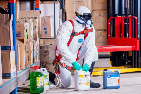 un applicateur en combinaison avec masque et lunette qui tient un produit chimique